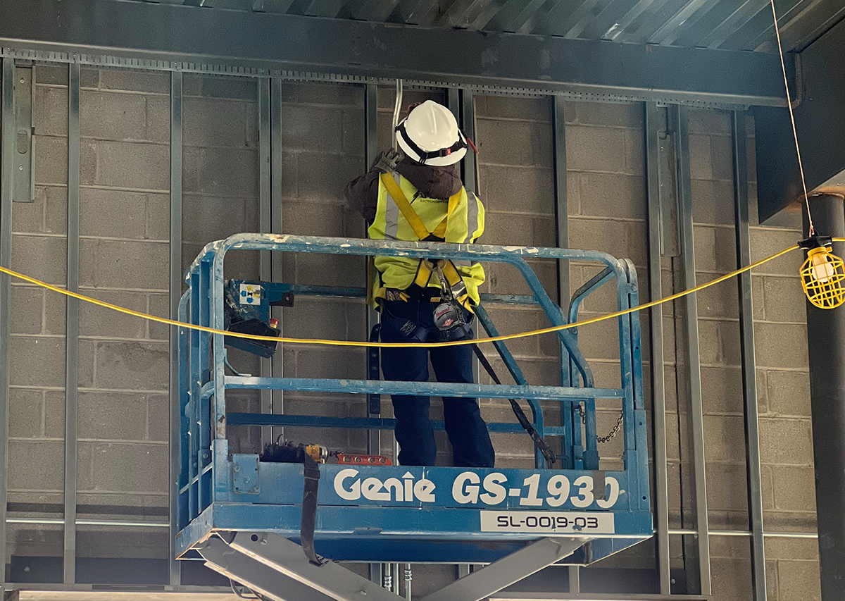 Worker in safety gear using a Genie GS-1930 lift to perform electrical installation in a commercial building under construction.